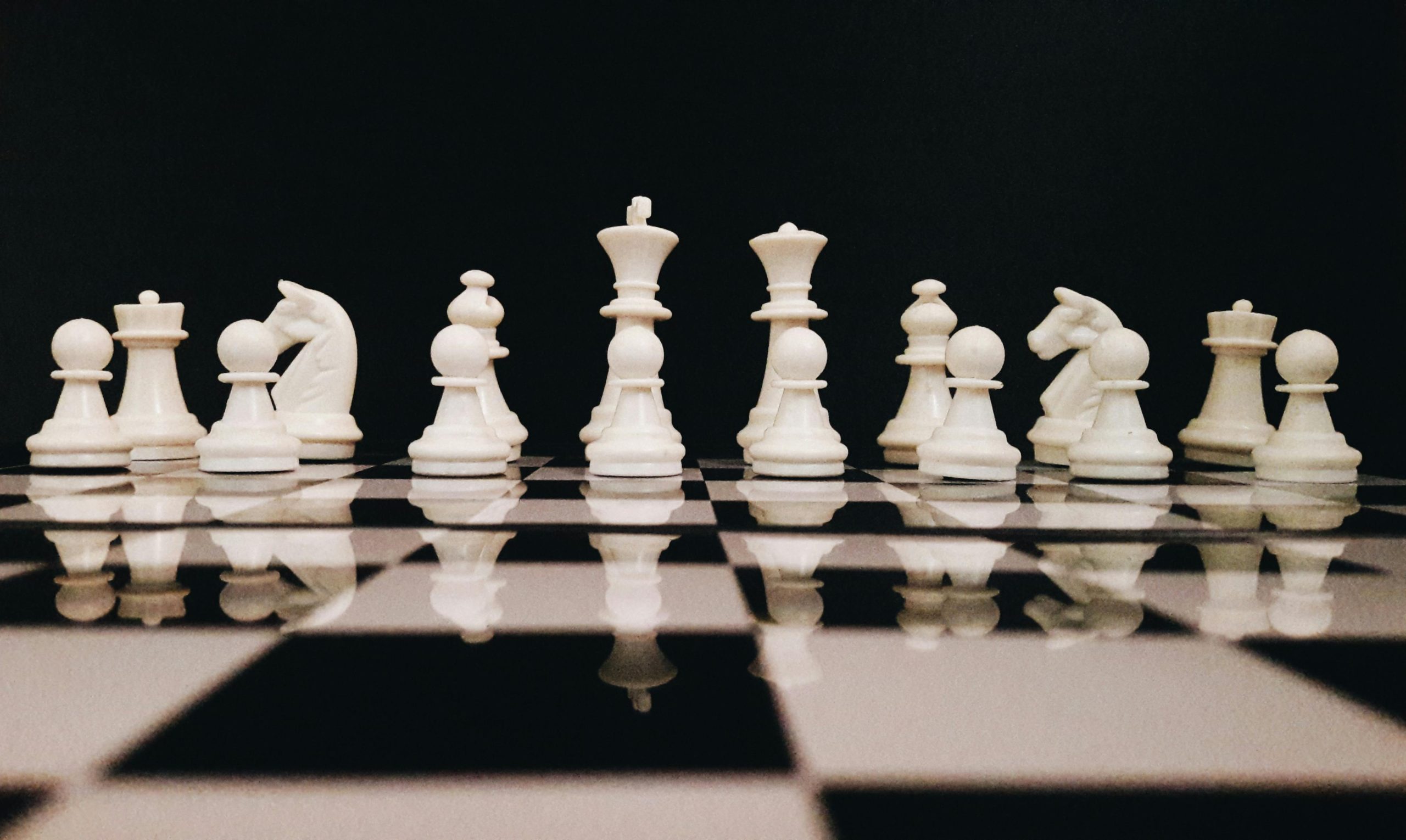 White chess pieces strategically placed on a board reflecting against a black background.